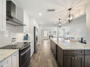 A modern kitchen with white cabinets, a stainless steel refrigerator, a built-in oven, and a large island with a marble countertop. - SaltRunner: Updated 3/2 home with Private Pool (St. Augustine)