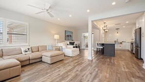 A modern living room with a beige sectional sofa, a white ottoman, and a ceiling fan. - SaltRunner: Updated 3/2 home with Private Pool (St. Augustine)