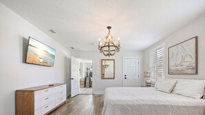 A bedroom with a large bed, a dresser, a chandelier, and artwork on the walls. - SaltRunner: Updated 3/2 home with Private Pool (St. Augustine)