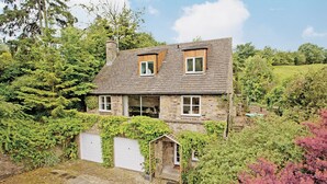 A stone house with a sloped roof, a garage, and a small porch.
