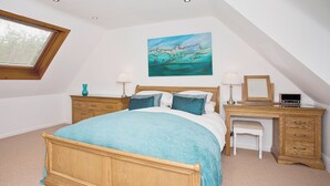 A bedroom with a bed, a desk, a chair, a window, and a painting on the wall.