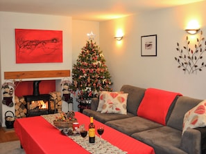 Un salón acogedor con chimenea, un árbol de Navidad y un sofá con cojines rojos.
