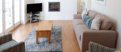 A living room with a sofa, two striped chairs, a wooden table, a TV, and artwork on the walls.