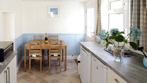 Une cuisine avec une table et des chaises en bois, un lave-vaisselle et une fenêtre avec des rideaux.