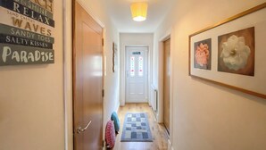 A hallway with a wooden floor, a door on the left, and a framed artwork on the right.
