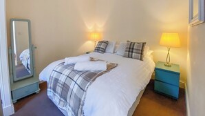 A neatly made bed with a plaid blanket, two bedside lamps, and a mirror on a dresser.