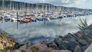 A marina with numerous boats docked, surrounded by rocky terrain and hills in the background.