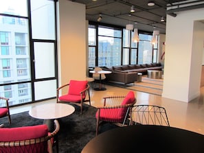 A modern lounge area with a sofa set, multiple chairs, and a round table. Large windows provide a view of the cityscape. - 1 Block to Pike Pl Market & Easy Walk to Stadium ~ Balcony with Water Views (Seattle)