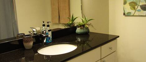 A bathroom with a black countertop sink, white cabinets, and a mirror above it. There are three lights above the mirror, and a towel hangs on the wall.