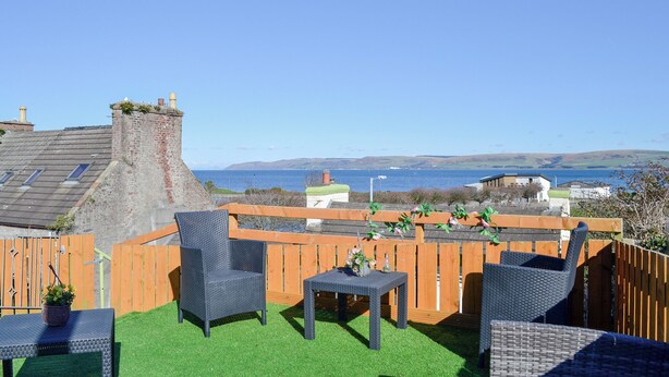 Una terraza en la azotea con muebles de mimbre, vista al mar y un paisaje montañoso distante.