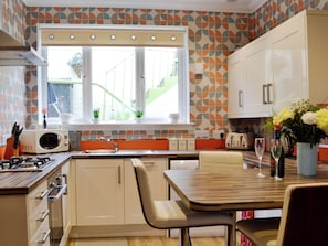 Una cocina con ventana, microondas, lavaplatos, armarios y una mesa de comedor con sillas.