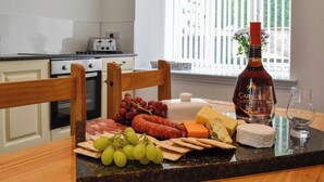 A kitchen with a dining table set for a meal, featuring a bottle of wine, glasses, cheese, meats, and grapes. - Kirroughtree Steading 1 - UK5859 (Newton Stewart)