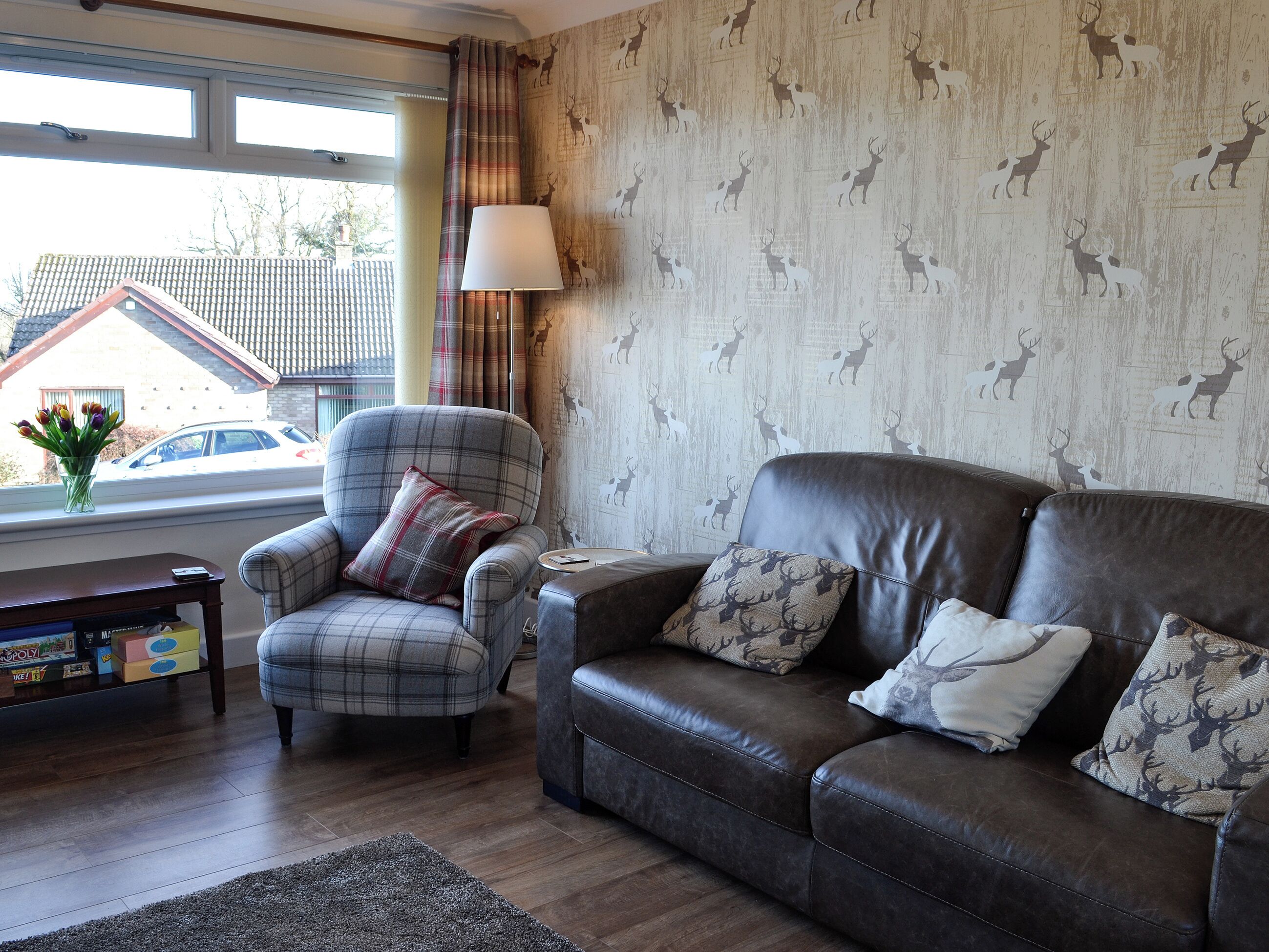 A living room with a plaid armchair, a leather sofa, and a patterned wallpaper.