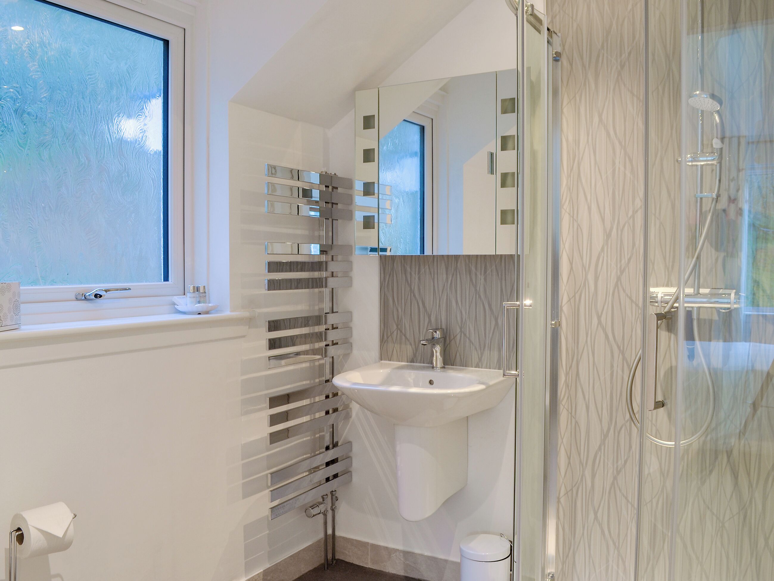 A modern bathroom with a glass shower enclosure, a white sink, and a window with frosted glass.
