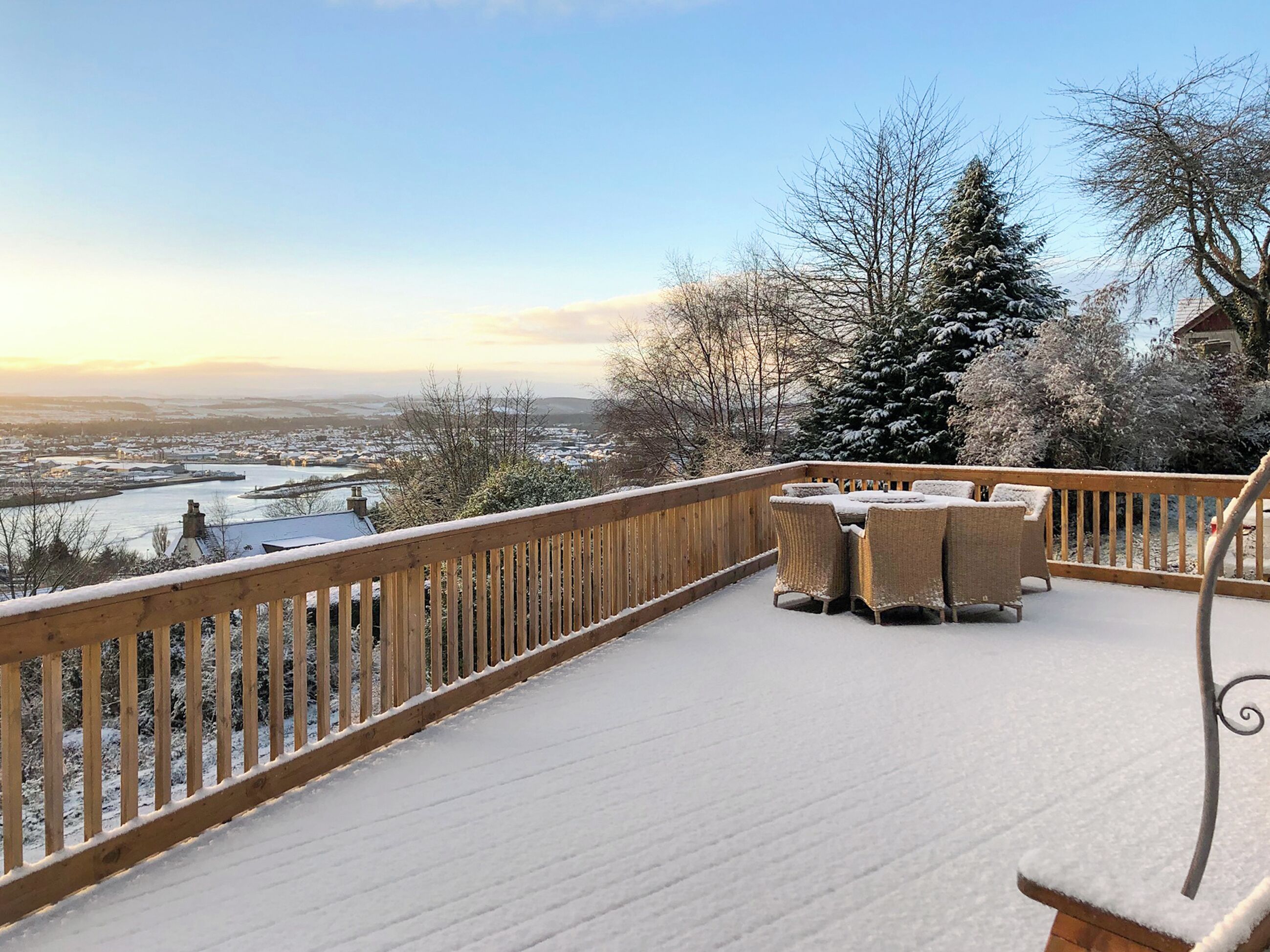 Une terrasse enneigée, meublée pour l’extérieur, offrant une vue sur une rivière et, au loin, sur le paysage urbain.