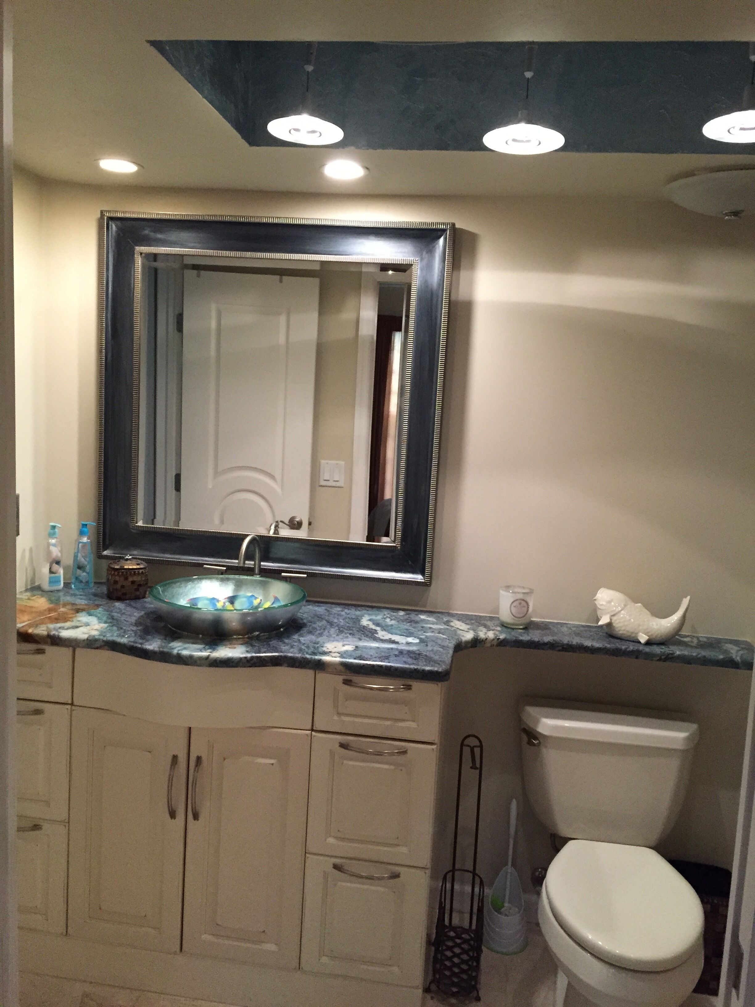 A bathroom with a marble countertop, a large mirror, a toilet, and a cabinet.