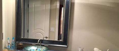 A bathroom with a marble countertop, a large mirror, a toilet, and a cabinet.