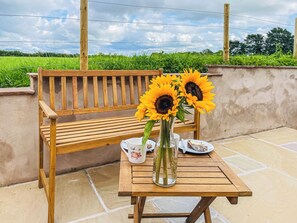 Un banc en bois, une table avec un vase rempli de tournesols et une assiette de nourriture.