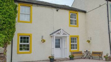 A building with a white exterior and yellow window frames, a white door, and a small porch with two benches and a table.