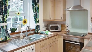 A kitchen with wooden cabinets, a microwave, an oven, a sink with a dish rack, and a window with curtains.