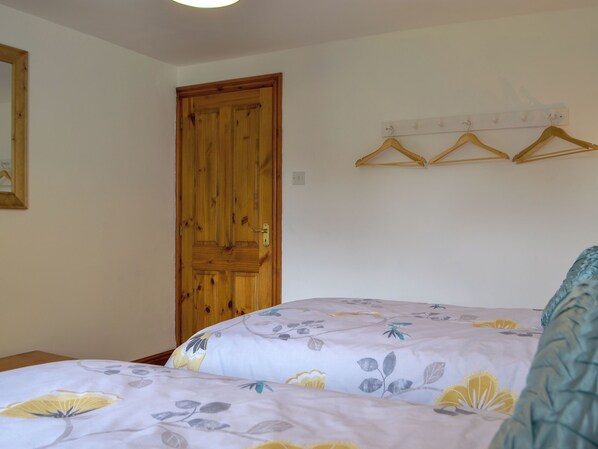 Une chambre avec deux lits, une porte en bois et un porte-vêtements fixé au mur.
