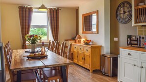 A dining area with a wooden table, chairs, a vase of flowers, and a view of the outdoors through a window. - 4 bedroom accommodation in Rhyduchaf, near Bala (Rhyduchaf, near Bala)