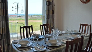 Un coin repas avec une table dressée pour quatre personnes, donnant sur un paysage verdoyant et offrant une vue sur la mer.