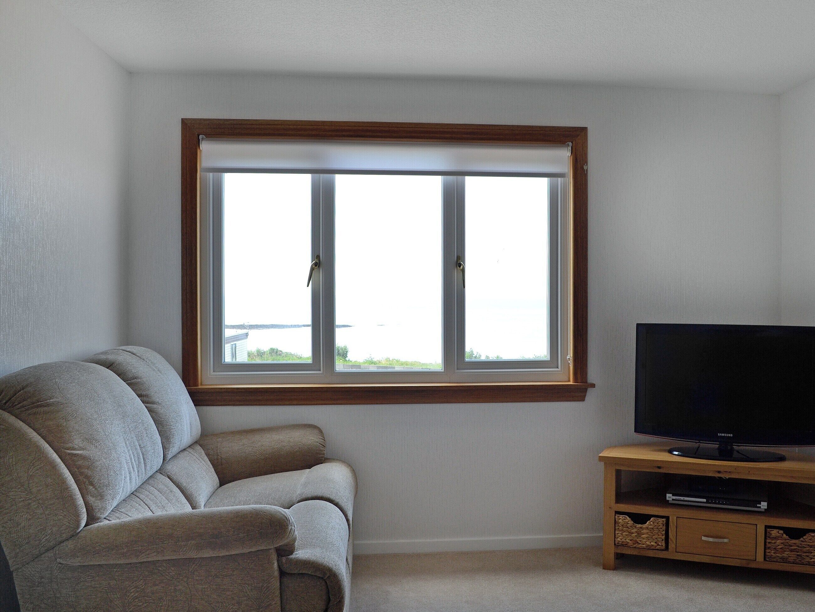 A living room with a grey sofa, a wooden TV stand with a flat-screen TV, and a window with blinds.