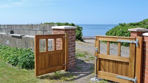 Une porte en bois qui mène à une zone de plage offrant une vue sur la mer.