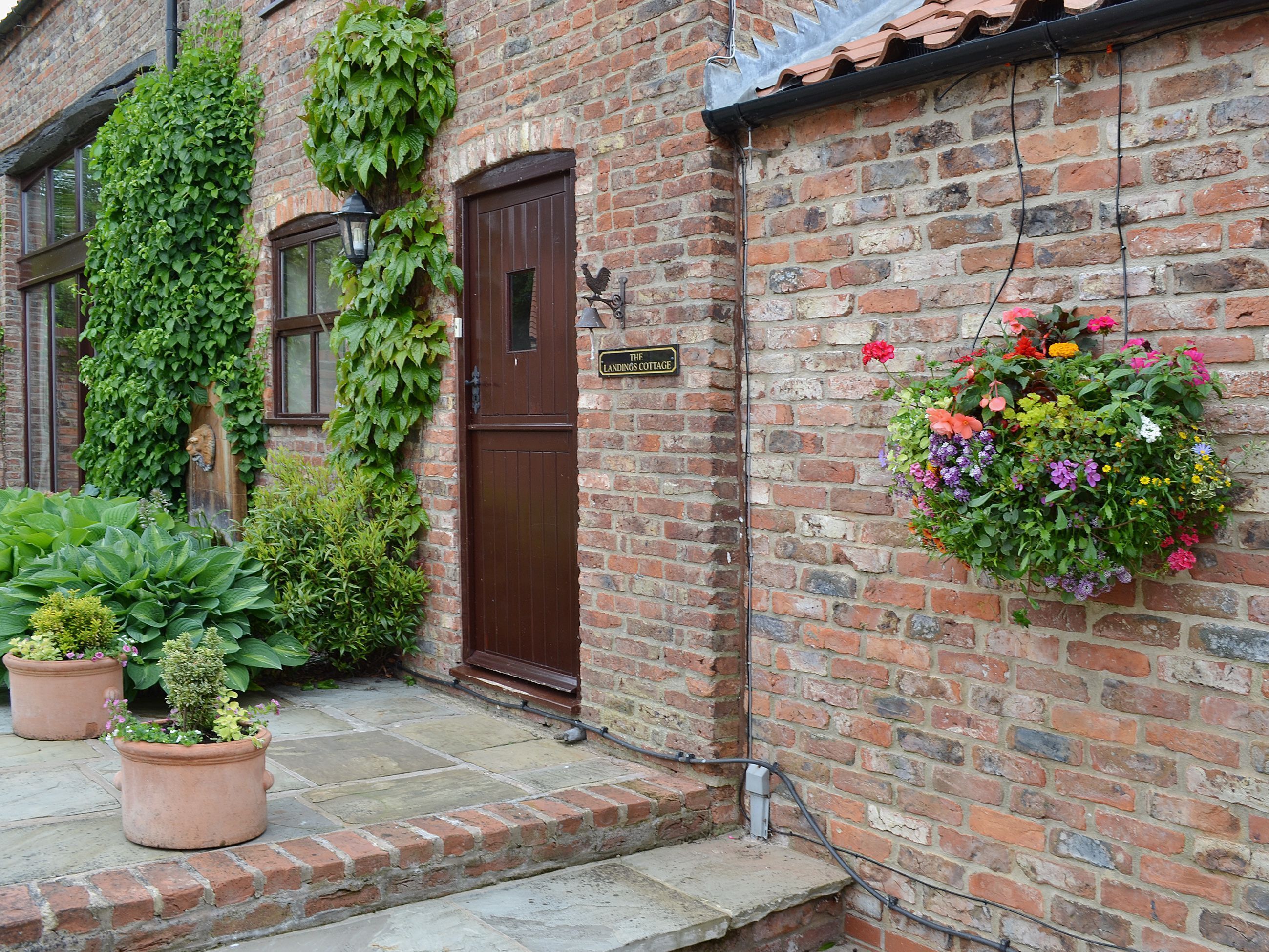 A brick building with a brown door, a hanging flower basket, and potted plants.