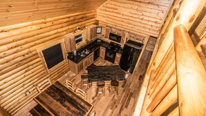 Ein Interieur einer Hütte mit Küchenbereich, ausgestattet mit Holzschränken, einer schwarzen Arbeitsplatte und einem Esstisch mit Hocker.
