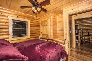 A log cabin bedroom with a bed, wooden walls, a ceiling fan, and a window with blinds. - Hocking Hills - Foxfire Cabin  > hiking, game room, fire pit, full kitchen, Wifi (Logan)