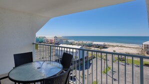 Ein Balkon mit Tisch und Stühlen, der Blick auf einen Strand mit Gebäuden im Hintergrund freigibt.