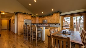 Een keuken met houten kasten, een roestvrijstalen koelkast en een eethoek met een houten tafel en stoelen.
