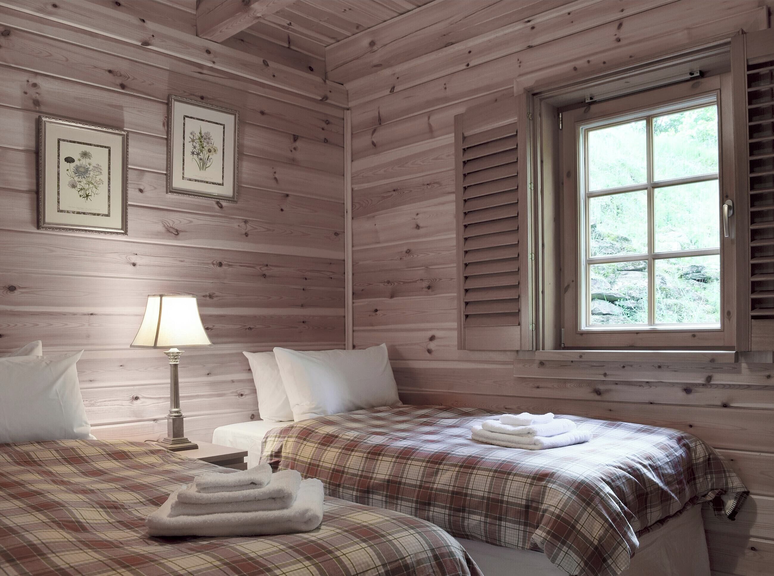 A wooden cabin room with two beds, a window, and framed botanical prints on the wall.