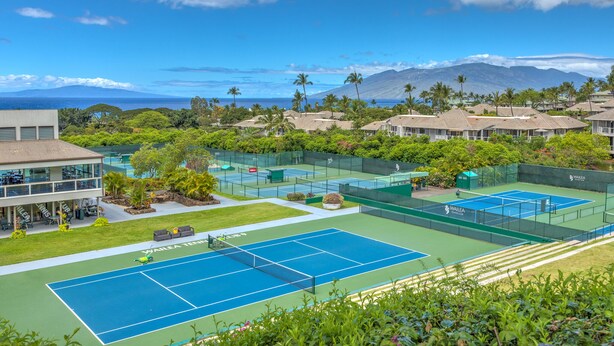 A tennis court with a pool, surrounded by lush greenery and a view of mountains. - Spacious End Unit (Kihei)