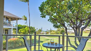 A balcony with two chairs and a table, overlooking a well-maintained lawn and a golf course. - Spacious End Unit (Kihei)