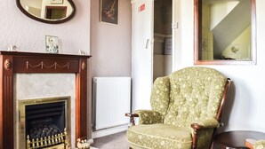 Una sala de estar con chimenea, un sillón verde, un espejo y una puerta que da a otra habitación.