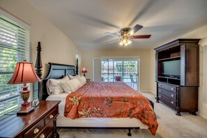 Un dormitorio con cama, ventilador de techo, mueble para televisión y ventana con persianas.