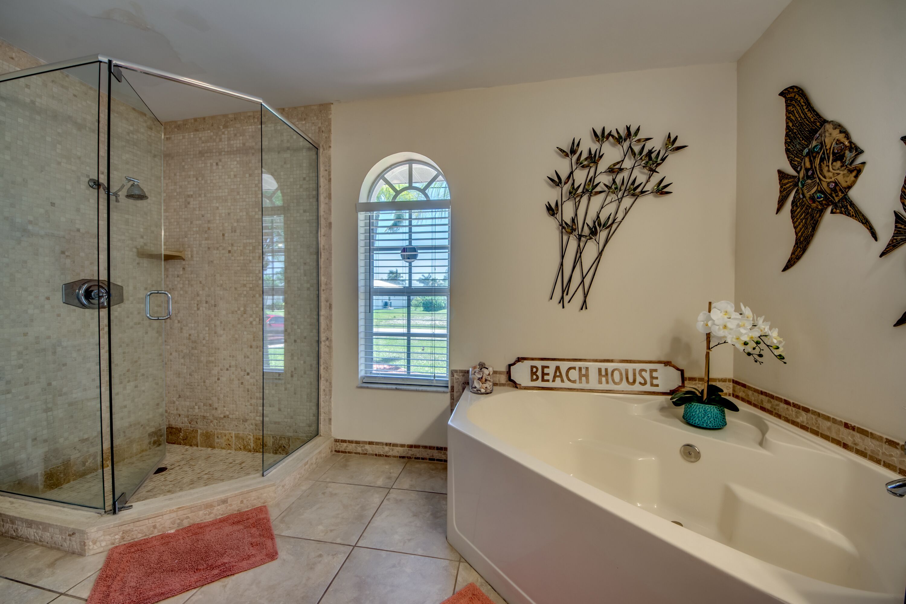 A bathroom with a glass-enclosed shower, a bathtub, and a window with a view of greenery.