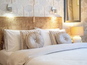 A neatly made bed with pillows, a headboard, and wall-mounted lighting.