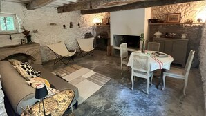 A rustic interior with exposed wooden beams, a stone wall, a fireplace, a dining area with a table and chairs, and a sofa with cushions. - OVERHANGING A RIVER, SHEPHERD'S HOUSE, AUTHENTIC, FAMILY-FRIENDLY, WIFI (Pieusse)