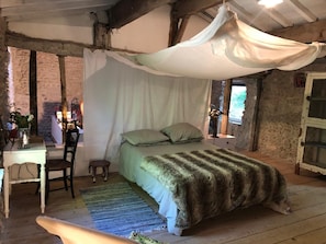 A rustic bedroom with a canopy bed, a small desk with a chair, and a stone wall. - OVERHANGING A RIVER, SHEPHERD'S HOUSE, AUTHENTIC, FAMILY-FRIENDLY, WIFI (Pieusse)
