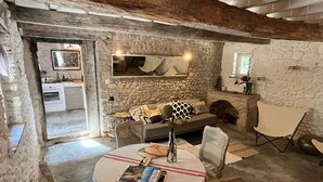 A rustic interior with a stone wall, a sofa, a dining table with a magazine, and a fireplace. - OVERHANGING A RIVER, SHEPHERD'S HOUSE, AUTHENTIC, FAMILY-FRIENDLY, WIFI (Pieusse)