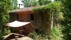 A rustic stone house with a tiled roof, surrounded by lush greenery and a red umbrella providing shade. - OVERHANGING A RIVER, SHEPHERD'S HOUSE, AUTHENTIC, FAMILY-FRIENDLY, WIFI (Pieusse)