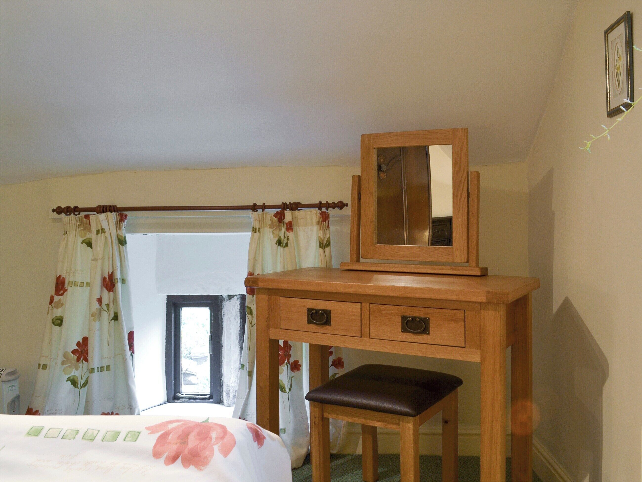 A bedroom with a wooden desk, a mirror, a bed with floral bedding, and a window with curtains.