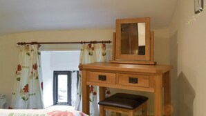 Quarto com escrivaninha de madeira, espelho, cama com roupa de cama florida e janela com cortinas.
