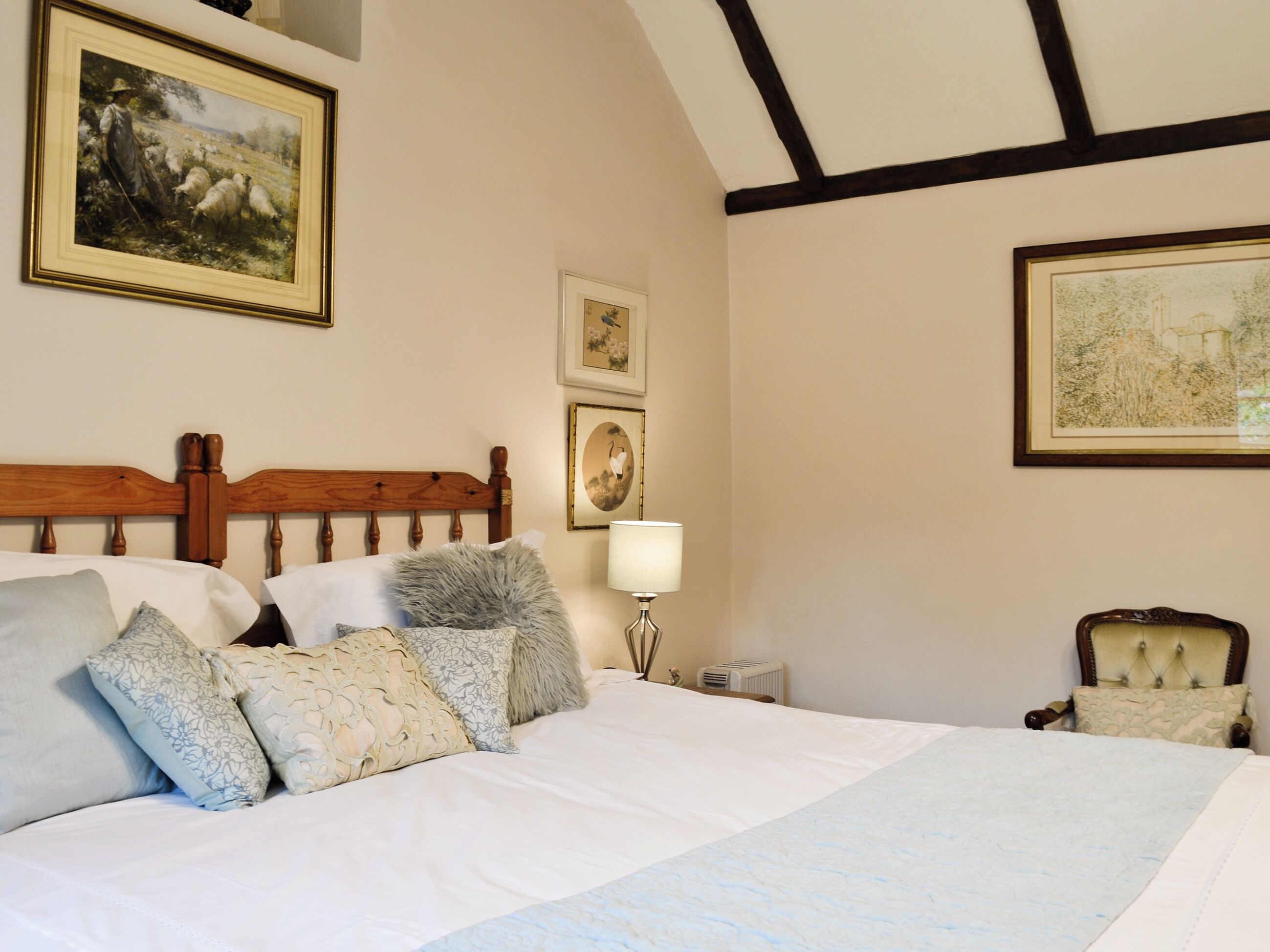 Une chambre à coucher avec une tête de lit en bois, un grand lit avec de nombreux oreillers, une table de chevet avec une lampe et des œuvres d’art encadrées accrochées aux murs.