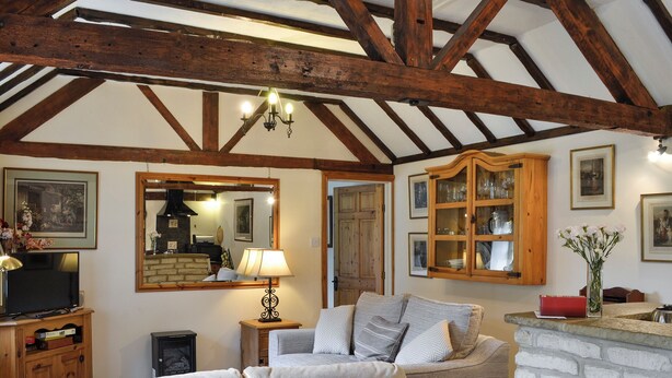 A cozy living room with a fireplace, a television, and a dining area with a stone wall. - 1 bedroom accommodation in Ampney Crucis, near Cirencester (Ampney Crucis, near Cirencester)