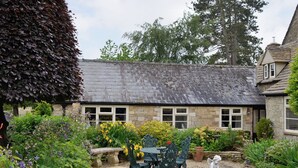 A stone building with a slate roof, surrounded by a garden with various plants and flowers. - 1 bedroom accommodation in Ampney Crucis, near Cirencester (Ampney Crucis, near Cirencester)